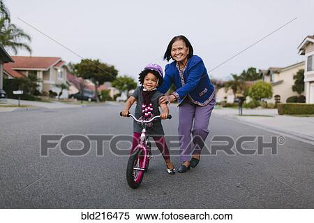 Stock Photography - Grandmother teaching granddaughter to ride bicycle on suburban street. Fotosearch