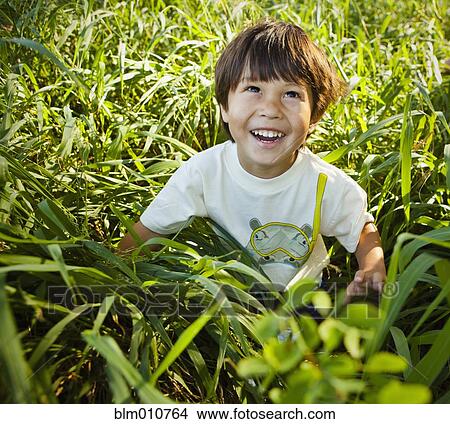 Picture - Grinning mixed race boy sitting in long grass. Fotosearch