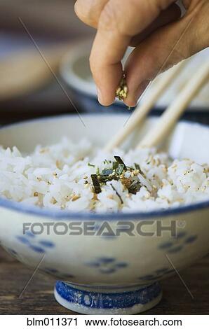 Stock Image - Hand putting seasoning on bowl of rice with chopsticks. Fotosearch