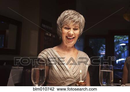 Stock Image - Happy woman blowing out birthday cupcake. Fotosearch