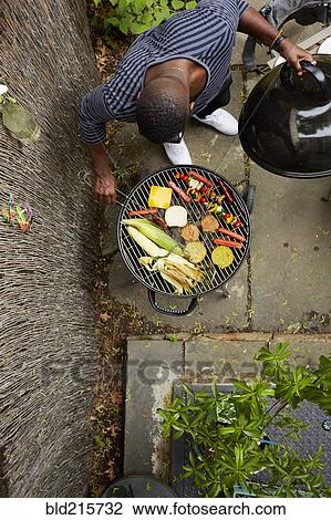 Stock Image - High angle view of African American man grilling at barbecue. Fotosearch