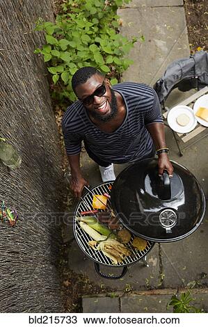 Stock Image - High angle view of African American man grilling at barbecue. Fotosearch