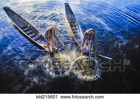 Stock Image - High angle view of Asian fishermen using fishing net in canoes on river. Fotosearch