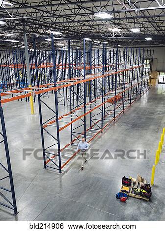 Stock Photograph - High angle view of Caucasian businessman walking in empty warehouse. Fotosearch