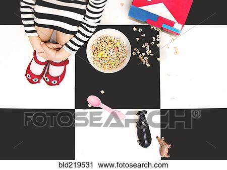 Stock Image - High angle view of girl spilling cereal on floor. Fotosearch