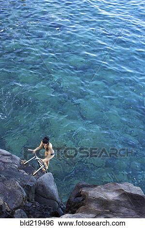 Stock Photograph - High angle view of woman climbing ladder out of ocean. Fotosearch