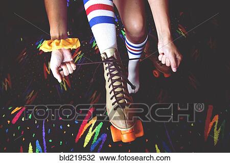 Stock Image - High angle view of woman lacing up roller-skates. Fotosearch