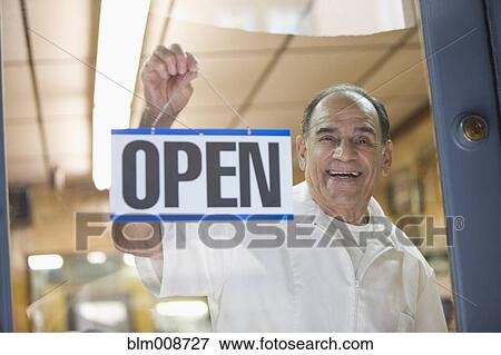 Stock Photo - Hispanic barber hanging open sign on barbershop door. Fotosearch