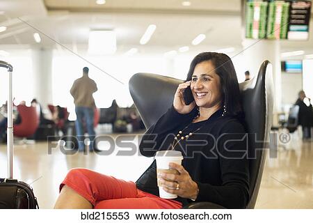 Stock Image - Hispanic businesswoman talking on cell phone in airport waiting area. Fotosearch