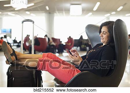 Stock Image - Hispanic businesswoman using cell phone in airport waiting area. Fotosearch
