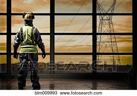 Stock Image - Hispanic construction worker looking out window at power lines. Fotosearch