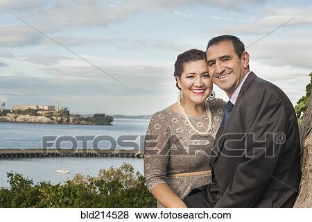 Stock Photo - Hispanic couple in formal wear smiling near waterfront. Fotosearch