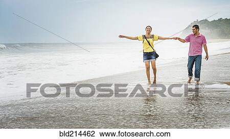 Stock Image - Hispanic couple playing in waves on beach. Fotosearch