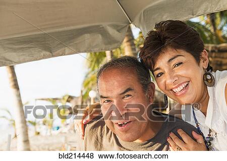 Hispanic couple smiling under umbrella on beach View Large Photo Image Stock Photo - Hispanic couple smiling under umbrella on beach. Fotosearch