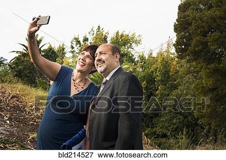 Stock Photo - Hispanic couple taking cell phone selfie in formal wear. Fotosearch