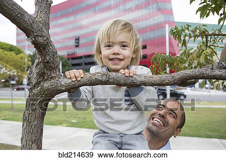 Stock Photo - Hispanic father and son playing on tree in park. Fotosearch