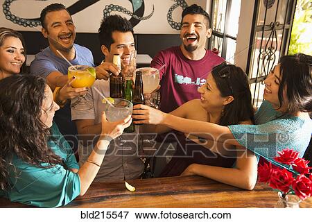 Stock Photo - Hispanic friends toasting with drinks at bar. Fotosearch