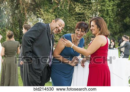 Stock Image - Hispanic friends using cell phone at wedding. Fotosearch