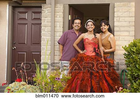 Stock Image - Hispanic girl dressed for quinceanera standing with parents. Fotosearch