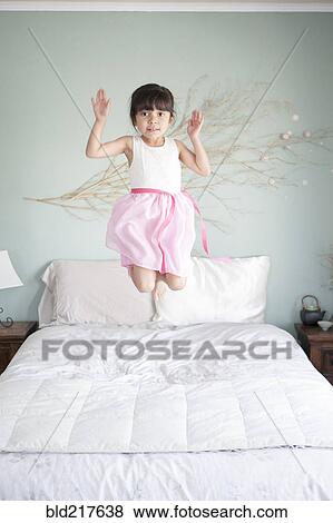 Stock Photo - Hispanic girl jumping on bed. Fotosearch