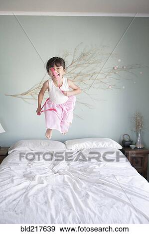 Stock Photo - Hispanic girl jumping on bed. Fotosearch