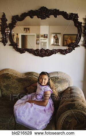 Stock Photo - Hispanic girl sitting on living room sofa. Fotosearch
