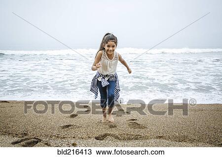 Stock Image - Hispanic girl walking barefoot on beach. Fotosearch