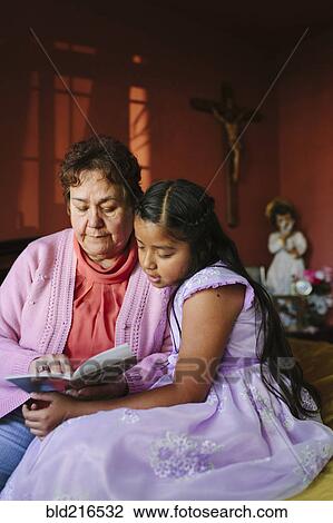 Stock Image - Hispanic grandmother and granddaughter ready book on bed. Fotosearch