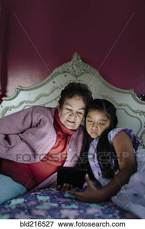 Hispanic grandmother and granddaughter using digital tablet on bed View Large Photo Image Stock Photo - Hispanic grandmother and granddaughter using digital tablet on bed. Fotosearch
