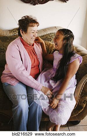 Stock Photo - Hispanic grandmother and granddaughter laughing on sofa. Fotosearch