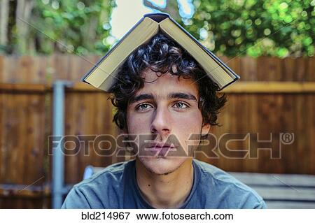 Stock Photo - Hispanic man balancing book on head in backyard. Fotosearch