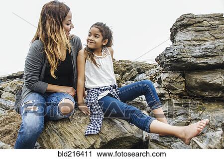 Stock Image - Hispanic mother and daughter sitting at tide pools. Fotosearch