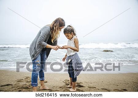 Stock Photography - Hispanic mother and daughter standing barefoot on beach. Fotosearch