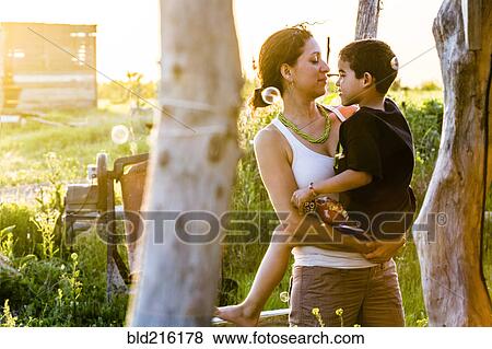 Stock Photo - Hispanic mother carrying son in garden. Fotosearch