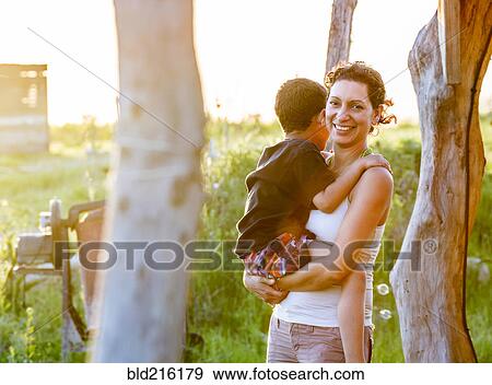 Stock Photo - Hispanic mother carrying son in garden. Fotosearch