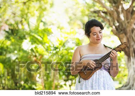 Picture - Hispanic musician playing ukulele in park. Fotosearch