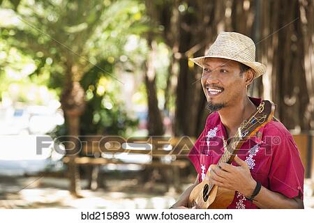 Stock Image - Hispanic musician playing ukulele in park. Fotosearch