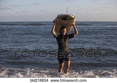 Picture - Hispanic surfer carrying surfboard in ocean. Fotosearch