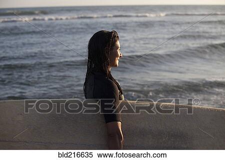 Stock Photography - Hispanic surfer carrying surfboard in ocean. Fotosearch