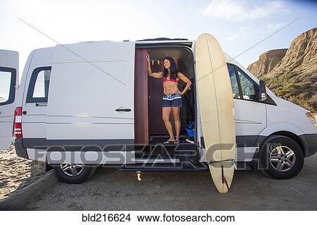 Picture - Hispanic surfer standing in van with surfboard. Fotosearch