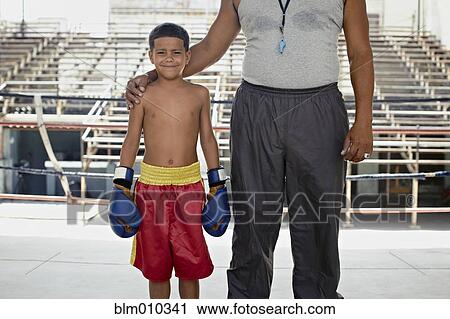 Stock Image - Hispanic trainer standing with boy in boxing gear. Fotosearch