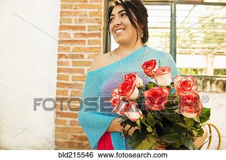 Stock Photograph - Hispanic woman carrying bouquet of roses outdoors. Fotosearch