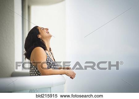 Stock Photography - Hispanic woman laughing near ocean hotel balcony. Fotosearch
