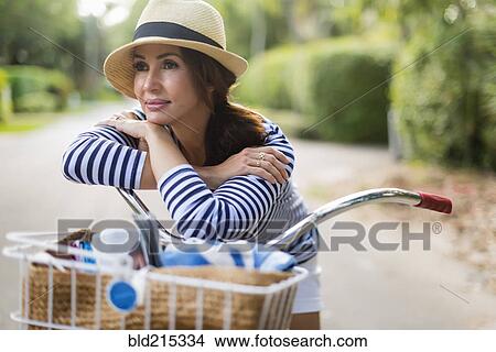 Hispanic woman leaning on bicycle on road View Large Photo Image Picture - Hispanic woman leaning on bicycle on road. Fotosearch