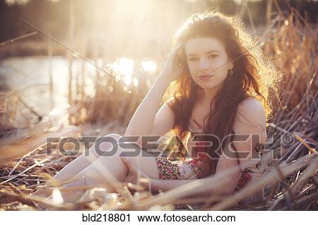 Stock Image - Hispanic woman sitting in tall grass in field. Fotosearch