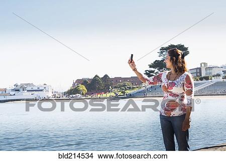 Hispanic woman taking cell phone selfie at waterfront View Large Photo Image Picture - Hispanic woman taking cell phone selfie at waterfront. Fotosearch