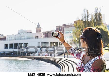 Stock Photography - Hispanic woman taking cell phone photograph of waterfront. Fotosearch