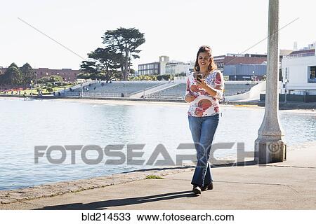 Stock Image - Hispanic woman texting on cell phone at waterfront. Fotosearch