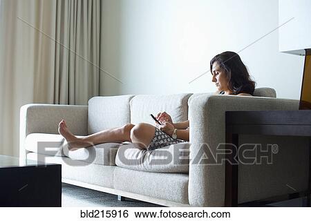 Stock Photograph - Hispanic woman using cell phone on hotel room sofa. Fotosearch