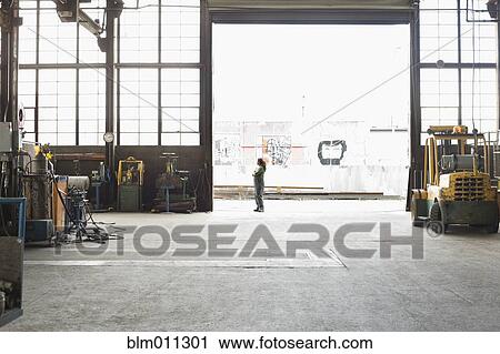 Stock Image - Hispanic worker standing in warehouse doorway. Fotosearch